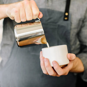 Barista ρίχνει γάλα από γυαλιστερή κανάτα από ανοξείδωτο ατσάλι, μέρος των Espresso Αξεσουάρ και Κανάτα Γάλακτος, όλα για τον καφέ.